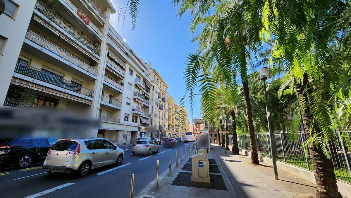 Perspective de la rue Arson à Nice : résidences à balcons et stores à gauche, palmiers et grille du jardin de la place Arson à droite