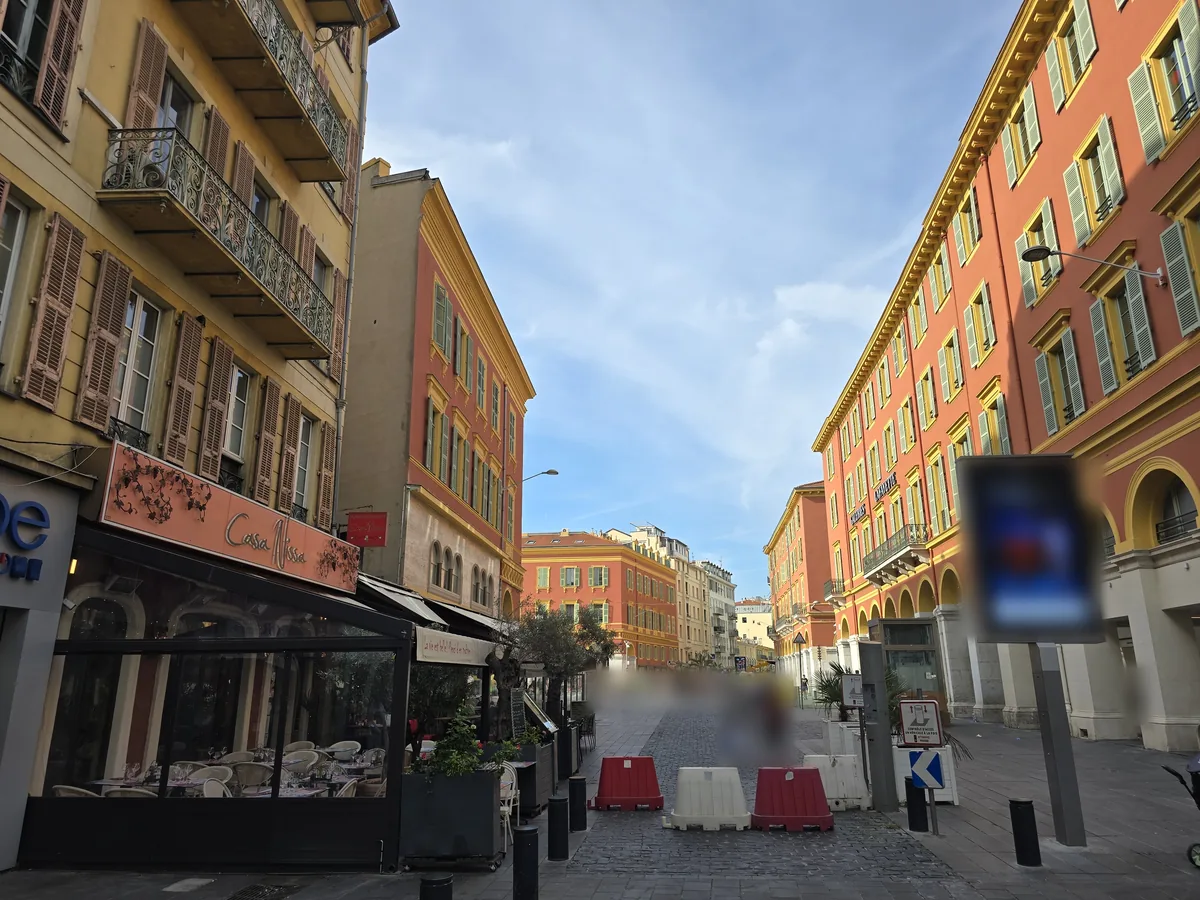 Débouché de la rue Gioffredo sur la place Masséna à Nice : façades rouges et ocre à volets verts, arcades et rue piétonne