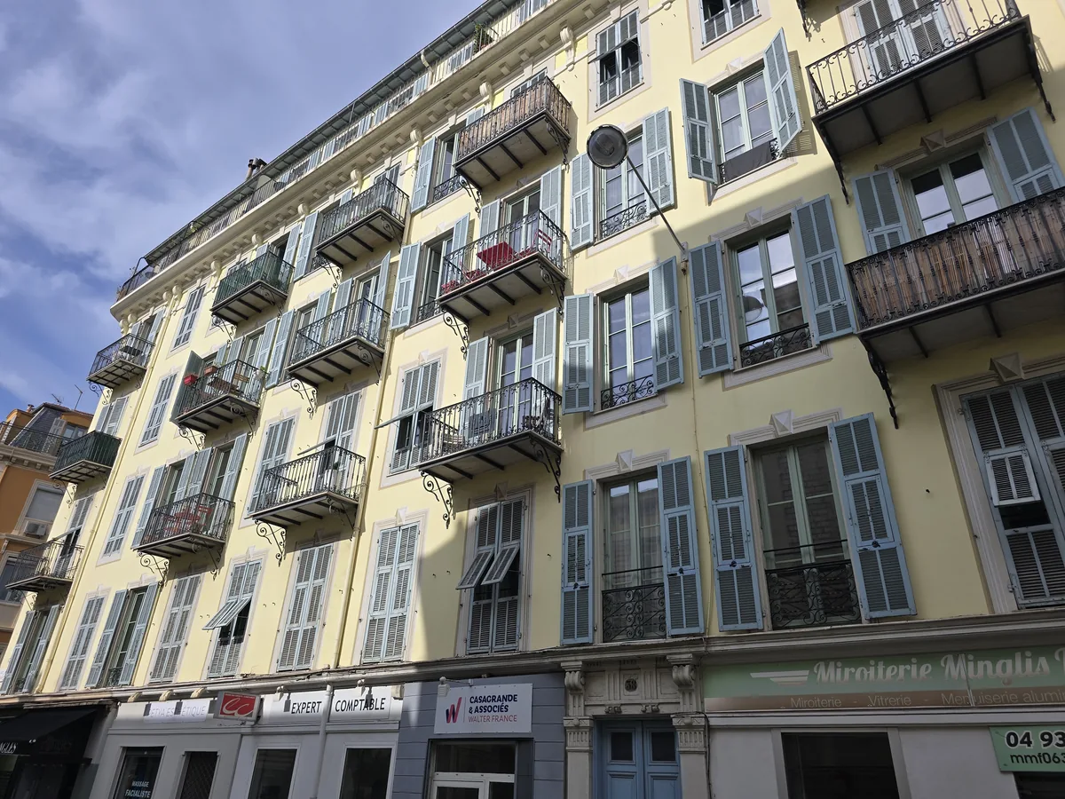Immeuble niçois Belle Époque à façade jaune pâle, volets bleu-gris et balcons en fer forgé, dans la partie centrale de la rue Gioffredo à Nice