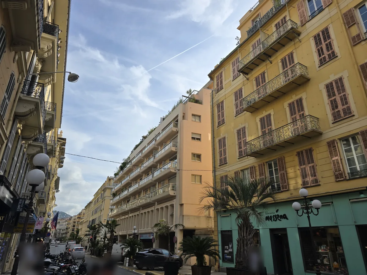 Rue Gioffredo à Nice côté place Masséna : façades ocre à balcons ouvragés, palmiers en bacs et immeuble à terrasses plantées en perspective