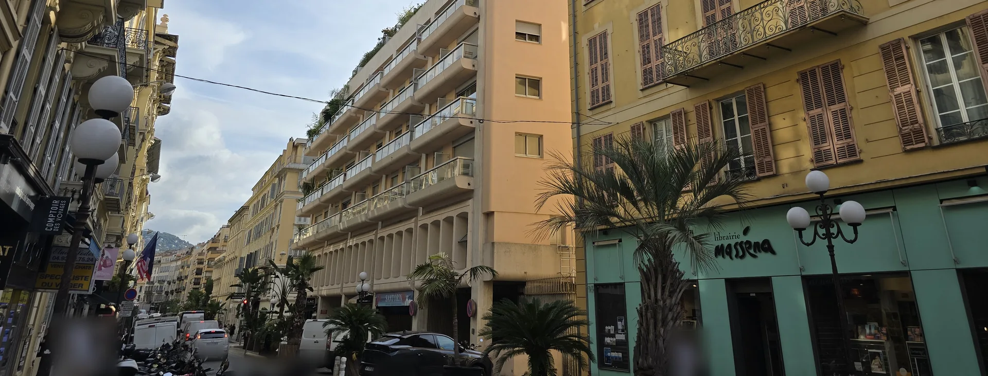 Rue Gioffredo à Nice côté place Masséna : façades ocre à balcons ouvragés, palmiers en bacs et immeuble à terrasses plantées en perspective