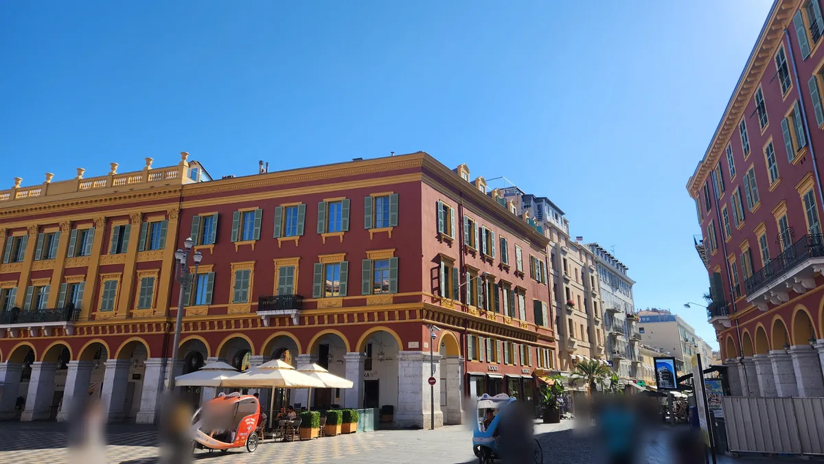 Place Masséna à Nice : immeubles rouges et ocre à arcades, parasols de terrasse et cyclo-pousse, à l'extrémité de la rue Gioffredo