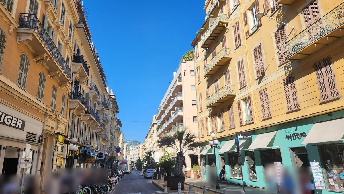Rue Gioffredo à Nice côté Masséna : immeubles ocre à balcons ouvragés, librairie, palmiers en bacs et résidence moderne en perspective