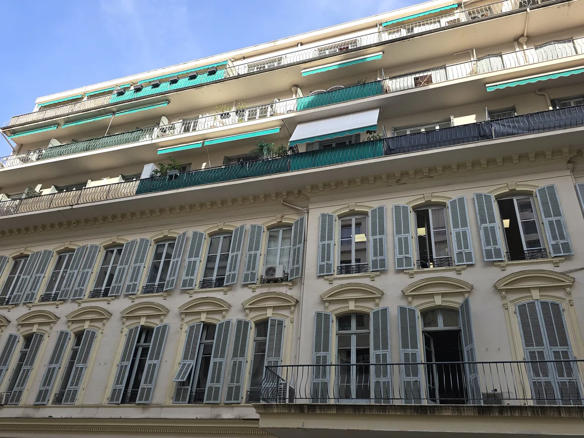 Immeuble ancien à volets gris surmonté d'étages en retrait avec terrasses et stores turquoise, rue de l'Hôtel-des-Postes à Nice