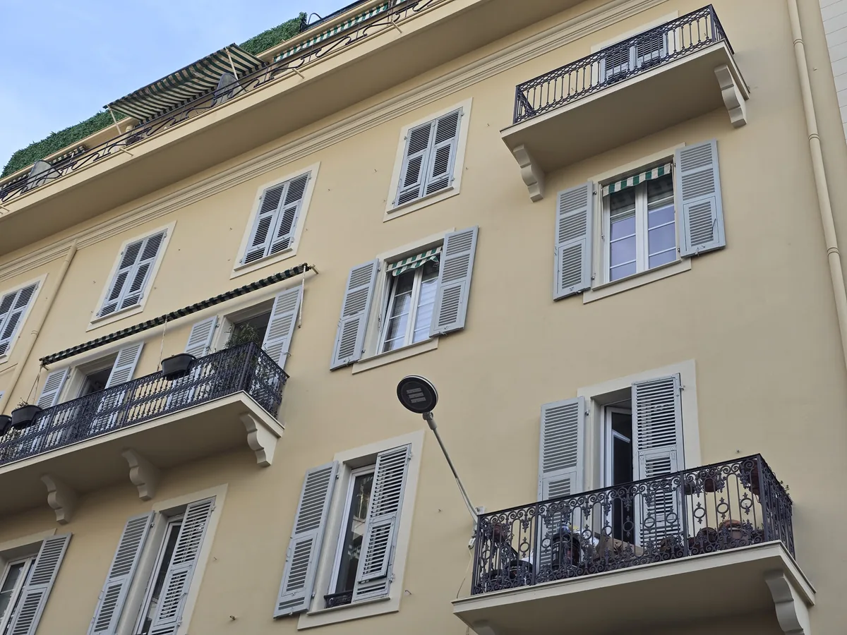 Façade ocre à volets gris et balcons en fer forgé d'un immeuble ancien, rue de l'Hôtel-des-Postes à Nice