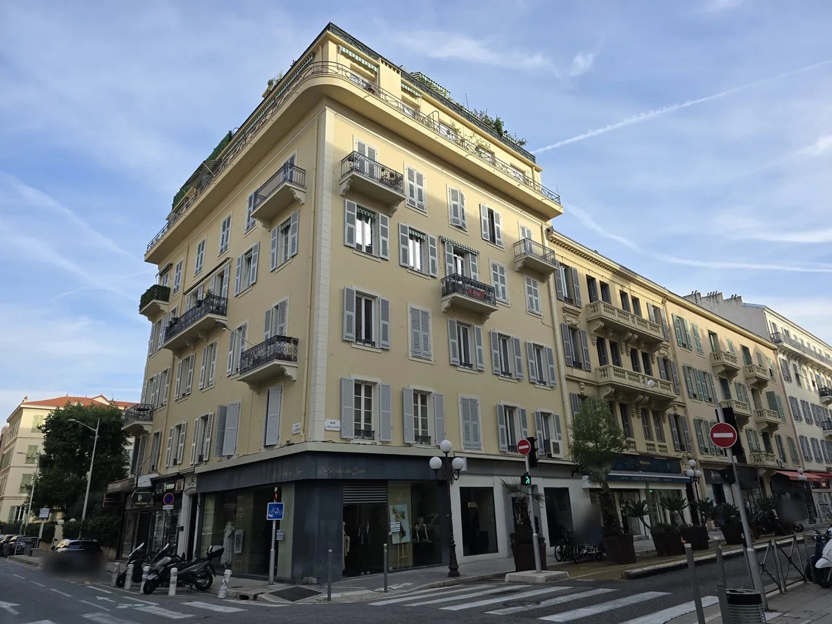 Immeuble niçois ancien d'angle, façade ocre, volets gris et balcons en fer forgé, rue de l'Hôtel-des-Postes à Nice