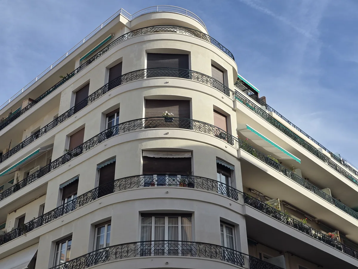 Immeuble blanc à angle arrondi, balcons en fer forgé et stores turquoise, au 32 rue de l'Hôtel-des-Postes à Nice
