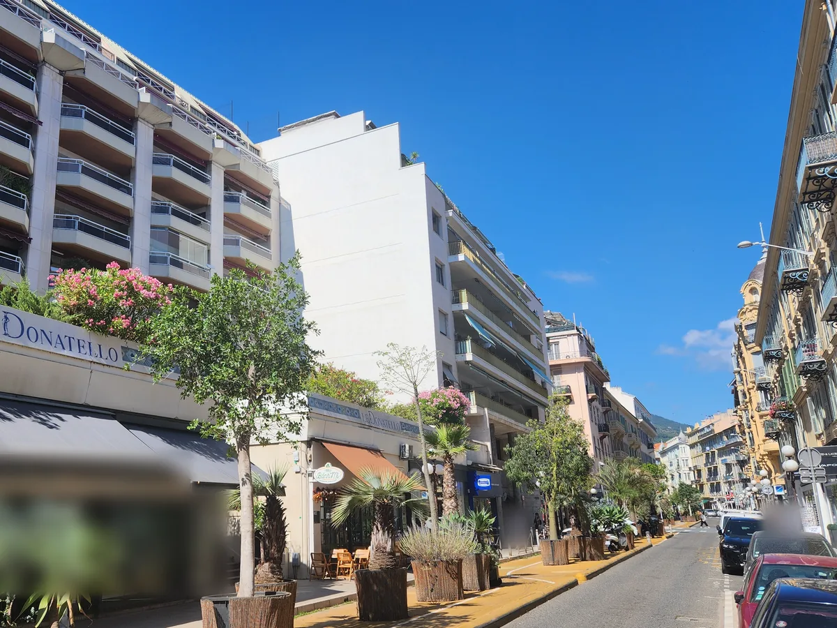 Rue de l'Hôtel-des-Postes à Nice : résidence Le Donatello, arbres et palmiers en bacs, voie cyclable jaune et immeubles anciens en perspective