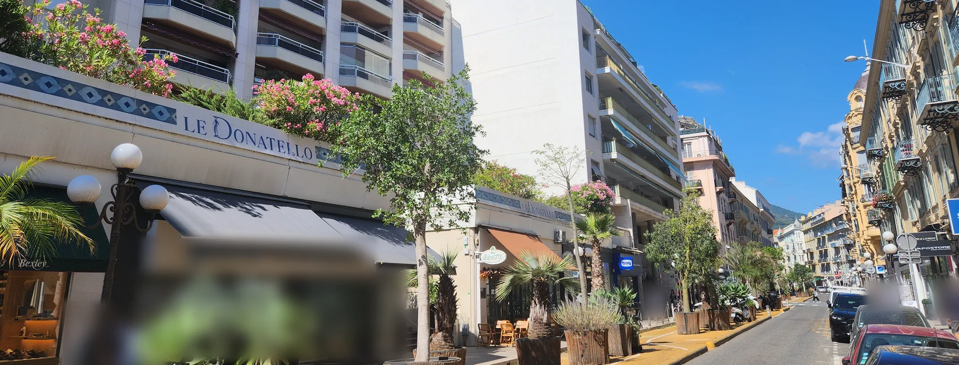 Rue de l'Hôtel-des-Postes à Nice : résidence Le Donatello, arbres et palmiers en bacs, voie cyclable jaune et immeubles anciens en perspective