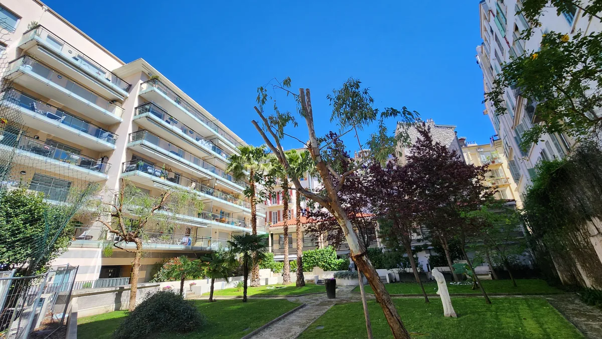 Jardin intérieur paysager de la résidence Jardin Pastorelli à Nice : pelouses, palmiers et façade à terrasses filantes vitrées