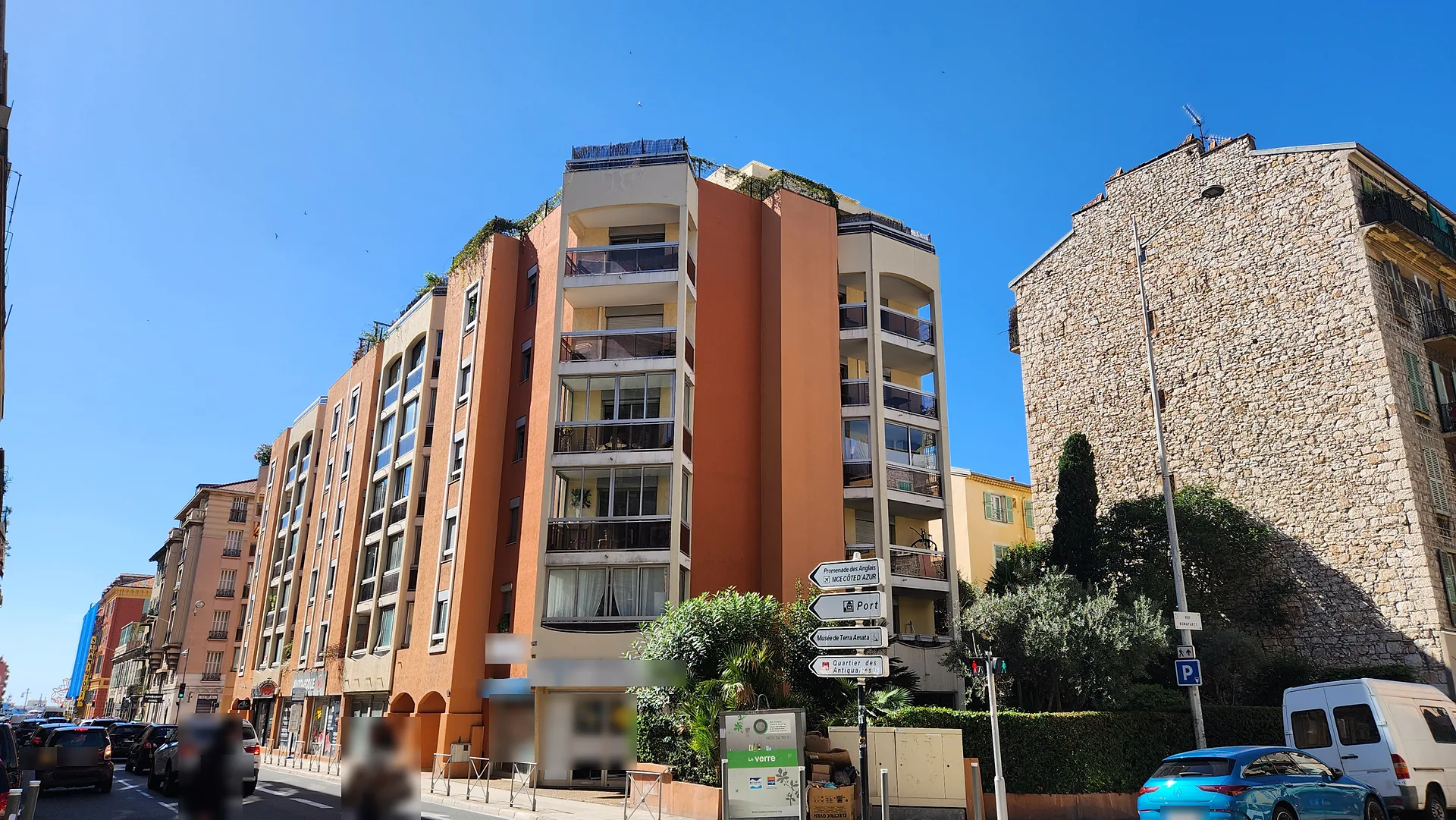 Résidence contemporaine orange à balcons et terrasses en attique végétalisées, à côté d'un haut pignon en pierre