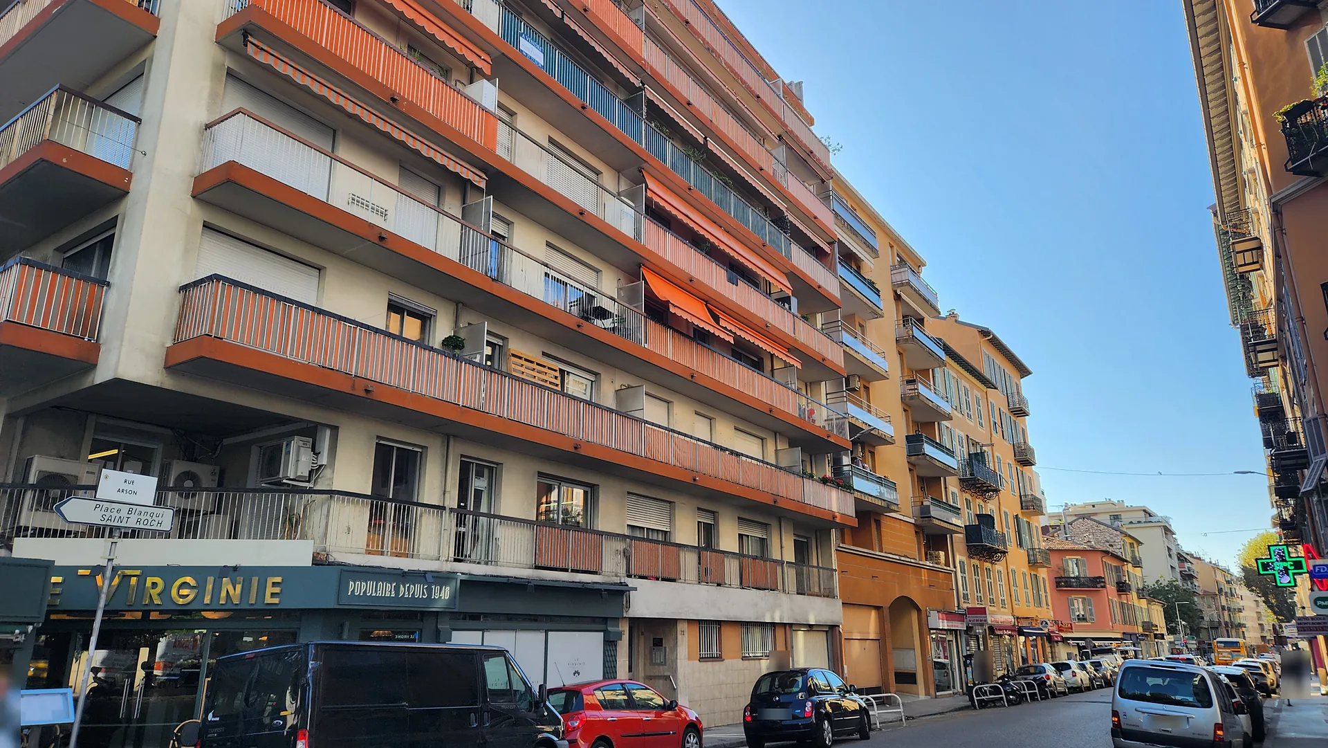 Résidence des années 1960 aux balcons filants à garde-corps orange au-dessus des commerces, rue Arson à Nice