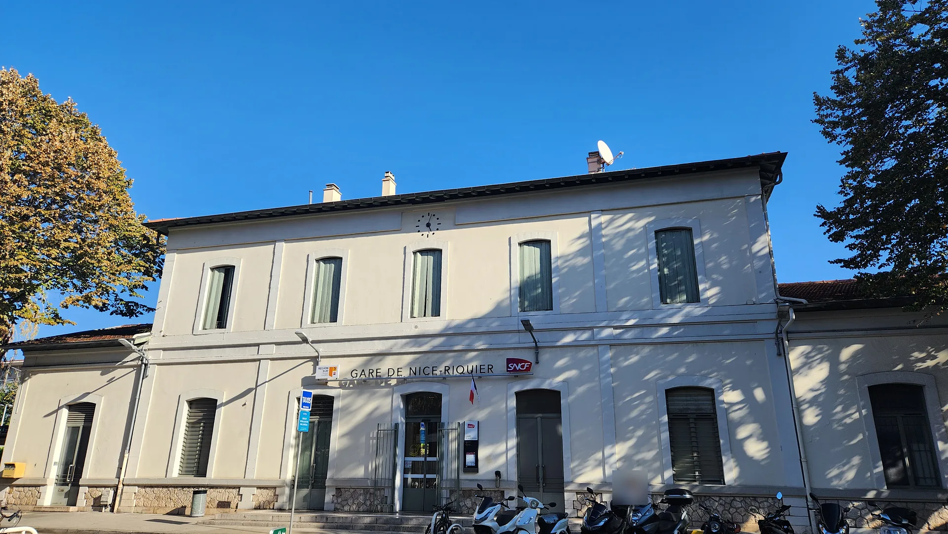 Bâtiment de la gare de Nice-Riquier, enseigne SNCF lisible, deux-roues stationnés devant